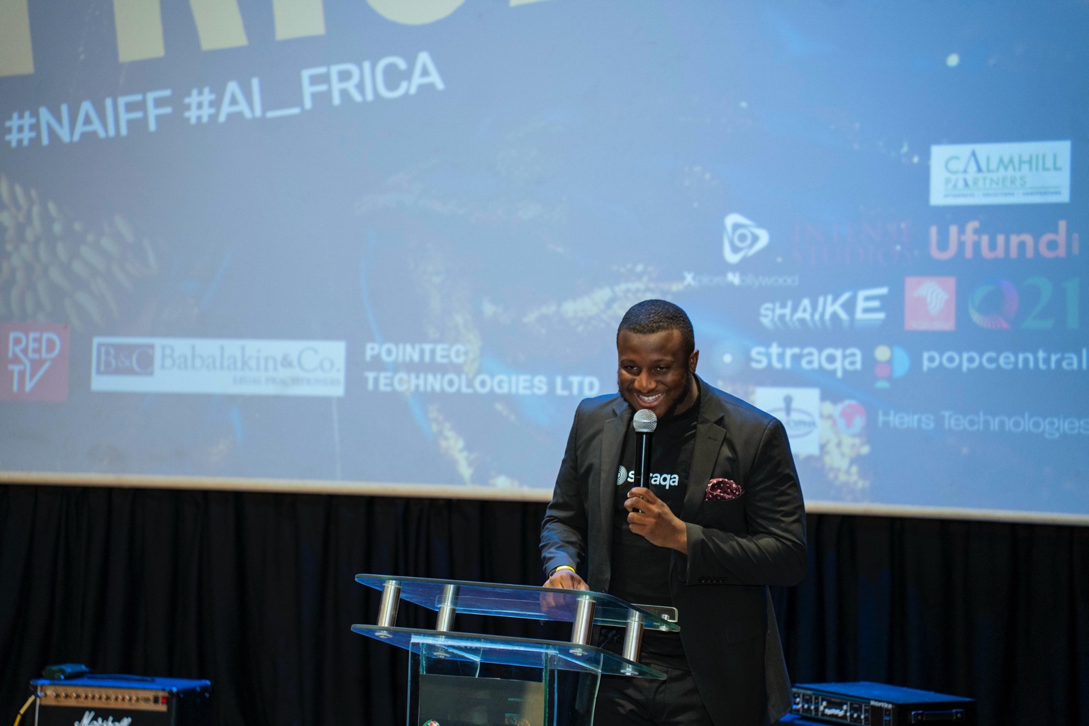 Precious Micah speaking at an event in a Straqa shirt